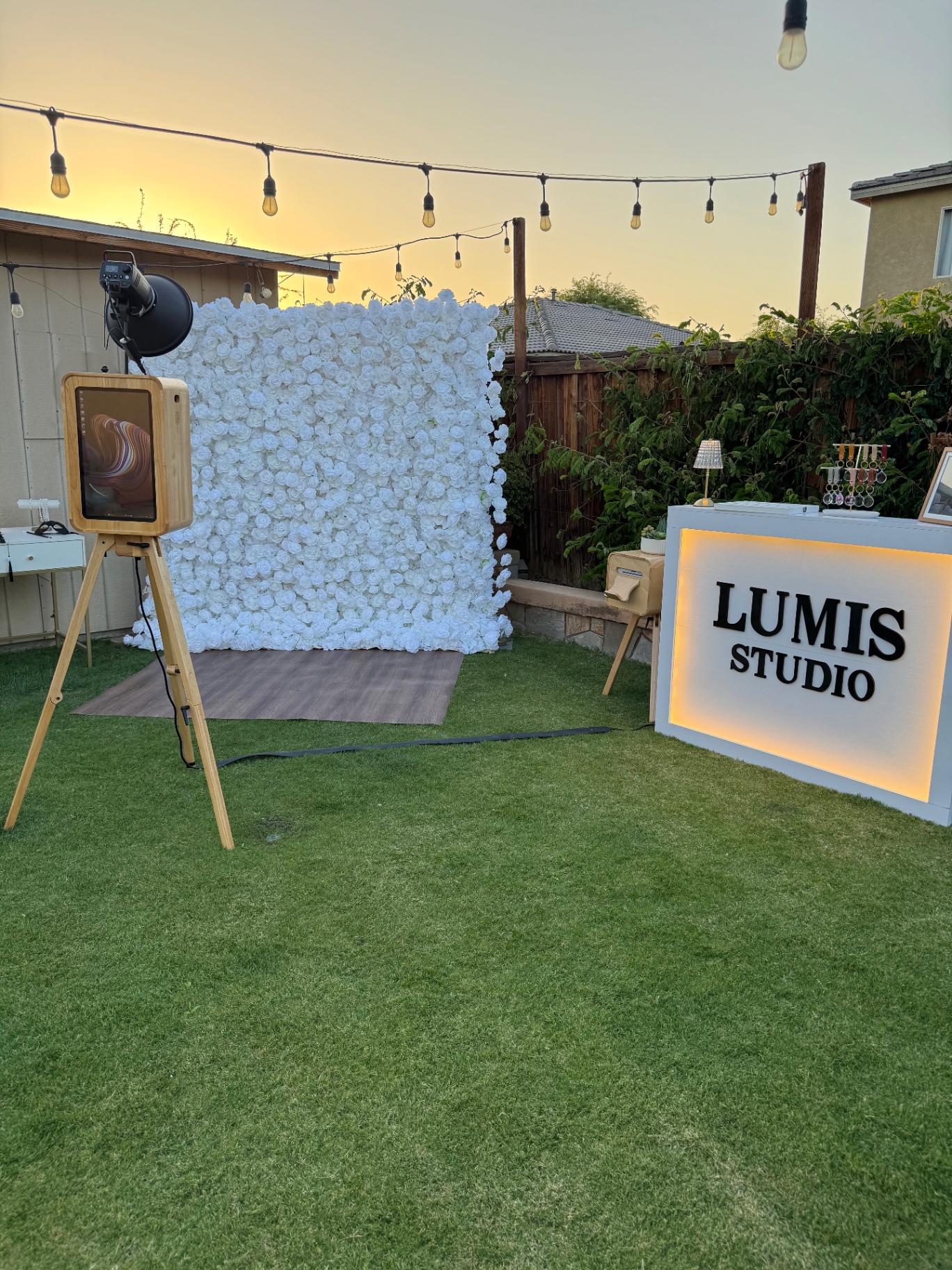 Lumis Studio photo booth setup at sunset with a white flower wall and illuminated Lumis Studio counter